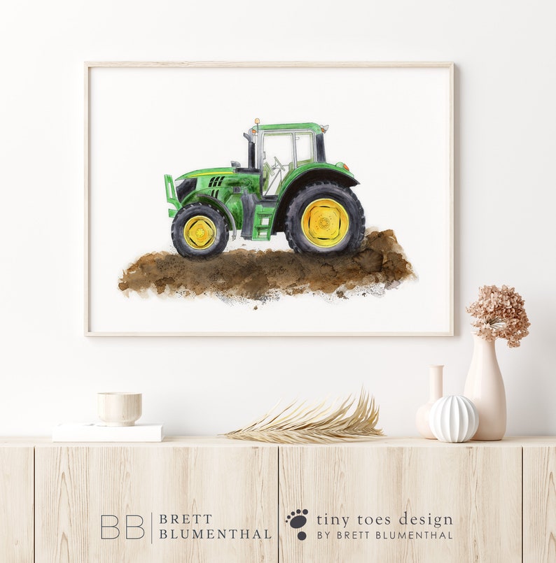 May include: Watercolor painting of a green tractor with yellow wheels, set against a white background. The tractor is depicted on a patch of brown soil. The artwork is framed in a light wood frame.