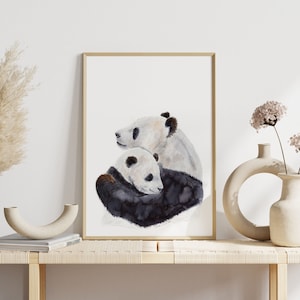 May include: A watercolor painting of two pandas hugging. The larger panda is white with black markings and is hugging a smaller panda. The smaller panda is white with black markings and has its head resting on the larger panda's shoulder. The painting is framed in a simple wooden frame.