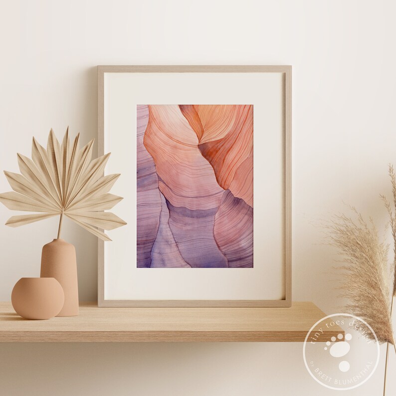 K&ouml;nnte beinhalten: Abstrakter Kunstdruck mit einer Nahaufnahme von geschichteten Felsformationen in Rosa-, Orange- und Lilat&ouml;nen. Der Druck ist in einem hellen Holzrahmen gerahmt.