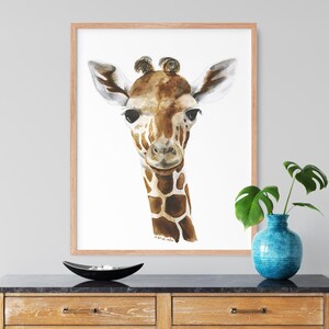 a framed painting of a giraffe's face, which is hanging on a wall above a wooden dresser. The dresser has a blue vase and a black bowl on it.