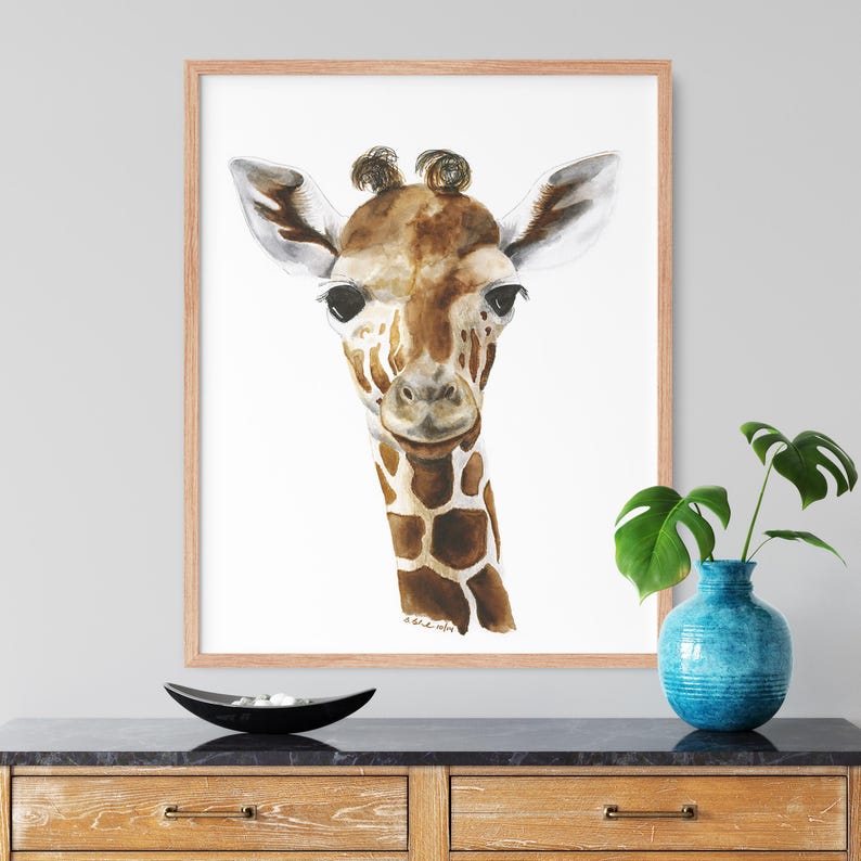 a framed painting of a giraffe's face, which is hanging on a wall above a wooden dresser. The dresser has a blue vase and a black bowl on it.