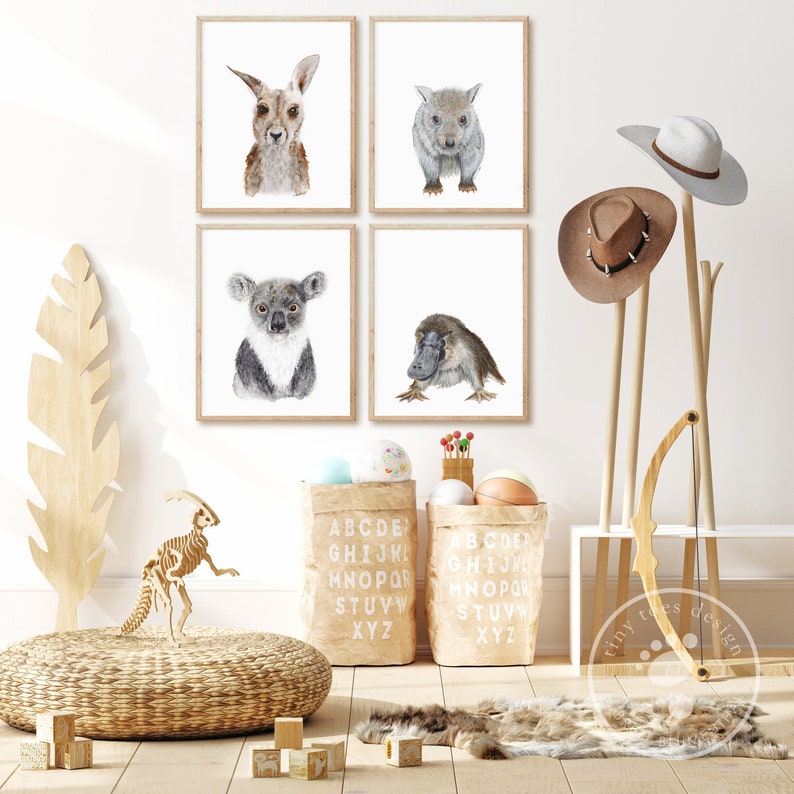 May include: Four framed watercolor illustrations of Australian animals: a kangaroo, a wombat, a koala, and a platypus. The prints are displayed on a white wall in a nursery setting with wooden toys and storage bins.