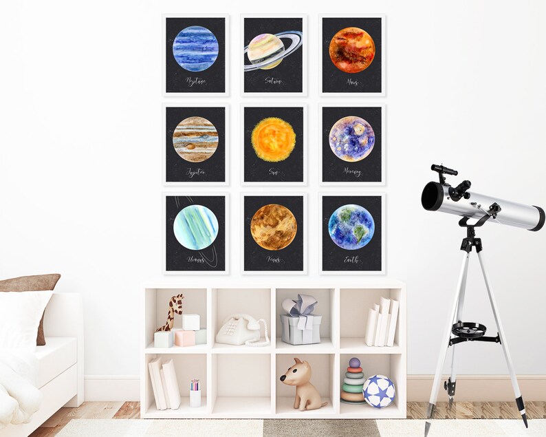 以下が含まれることがあります： 白い壁に、白い額縁に入った太陽系の惑星の水彩画が9枚飾られています。惑星は、海王星、土星、火星、木星、太陽、水星、天王星、金星、地球です。絵画は3行3列に配置されています。画像の右下には、銀色の望遠鏡が三脚に載っています。