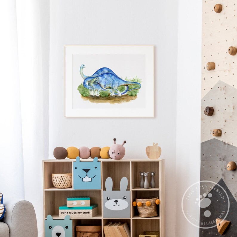 May include: A watercolor painting of two blue dinosaurs, a larger one with a smaller one following behind. The dinosaurs are walking through a green field. The painting is framed and hanging on a white wall.