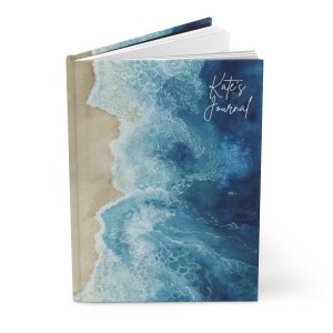 May include: A blue and white watercolor journal with a beach scene on the cover. The text "Kate's Journal" is written in white on the cover.