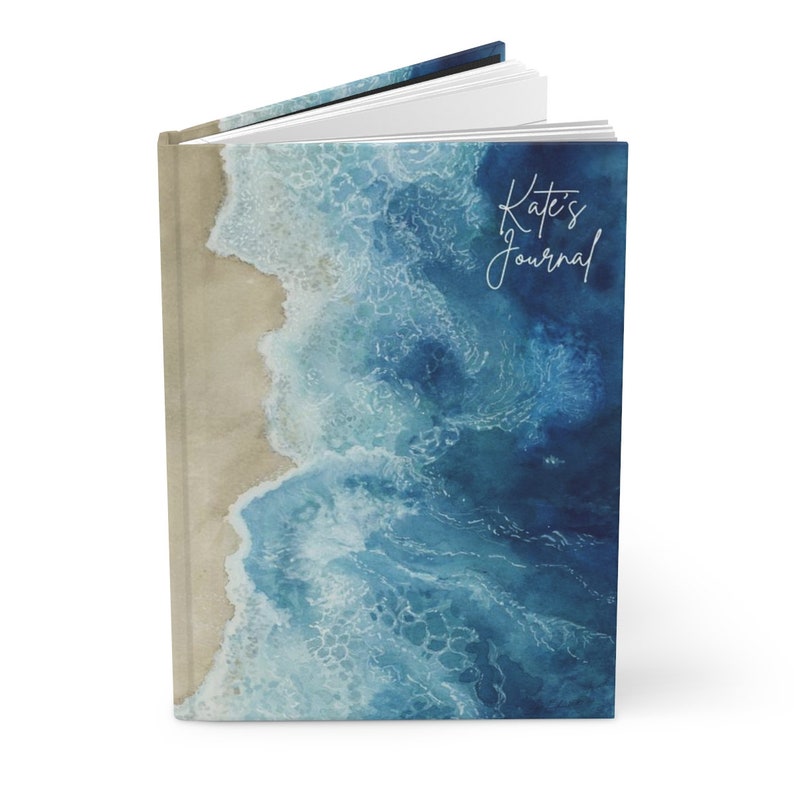 May include: A blue and white watercolor journal with a beach scene on the cover. The text "Kate's Journal" is written in white on the cover.