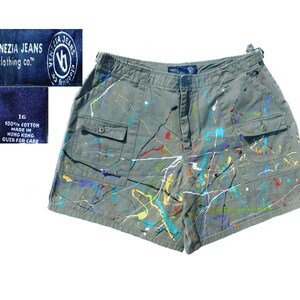 May include: Olive green shorts with colorful paint splatter design. The shorts have two front pockets and a button closure. The tag reads "VENEZIA JEANS clothing co." and "100% COTTON MADE IN HONG KONG". Size 16.