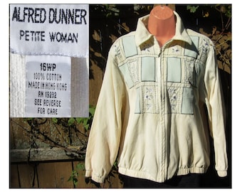 May include: A cream-coloured zip-up jacket with embroidered details. The jacket has light blue rectangular patches with floral and geometric embroidery. The label reads "ALFRED DUNNER PETITE WOMAN 16WP 100% COTTON MADE IN HONG KONG RN 19232 SEE REVERSE FOR CARE."