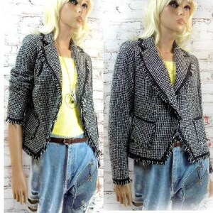 May include: A black and white tweed blazer with frayed edges and black trim. The blazer is paired with a yellow top, blue jeans, and a brown belt. The mannequin is wearing a necklace.