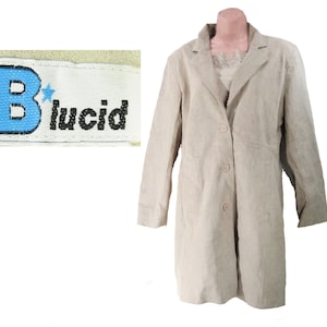 Peut inclure: Un long manteau en daim beige avec une fermeture boutonnée et deux poches. Le manteau porte une étiquette indiquant "B*lucid".