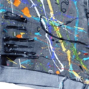 May include: Gray denim shorts with paint splatters in various colors, including yellow, blue, green, orange, and white. The shorts have several distressed areas with frayed edges.