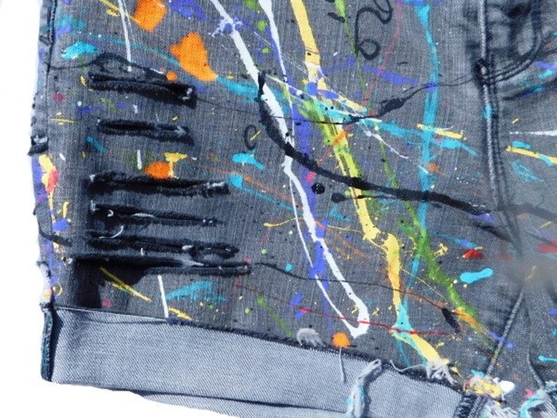 May include: Gray denim shorts with paint splatters in various colors, including yellow, blue, green, orange, and white. The shorts have several distressed areas with frayed edges.