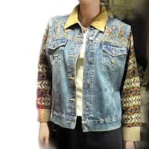 May include: A blue denim jacket with embroidered floral details on the front and a brown suede collar. The sleeves are made of a colorful knitted fabric with a geometric pattern.