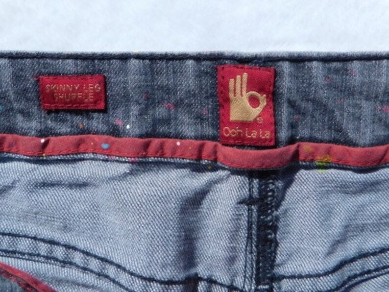 May include: Blue denim jeans with a red waistband and two red labels. The labels say "Skinny Leg Shuffle" and "Ooh La La".