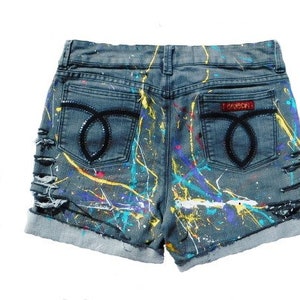 May include: Distressed denim shorts with paint splatters in various colors, including yellow, blue, and purple. The shorts have a back pocket with a black "FOREVER" label.