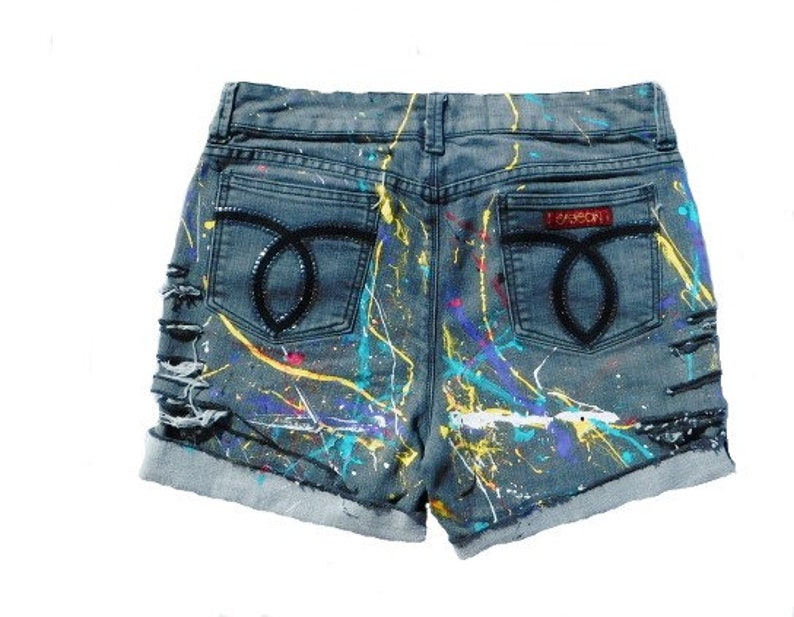 May include: Distressed denim shorts with paint splatters in various colors, including yellow, blue, and purple. The shorts have a back pocket with a black "FOREVER" label.