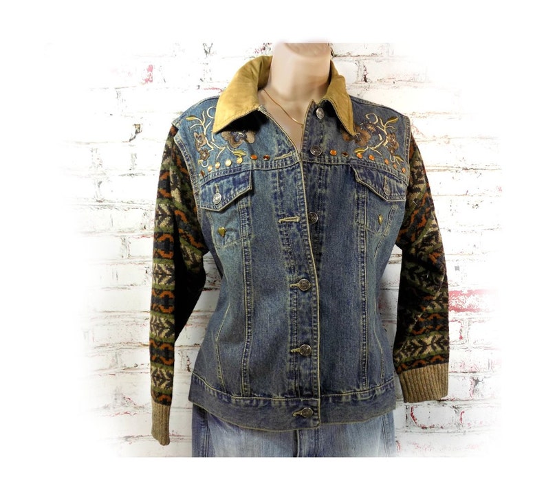 May include: A blue denim jacket with a brown suede collar and embroidered floral details on the sleeves. The sleeves are made of a brown, green, and orange patterned knit fabric.