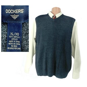 May include: A dark blue knitted sweater vest with a V-neck. The vest is made of 100% acrylic and has a label that reads "DOCKERS XL/XG 100% ACRYLIC/ACRILICO MADE IN CHINA HECHO EN CHINA RN 15610 REVERSE FOR CARE".