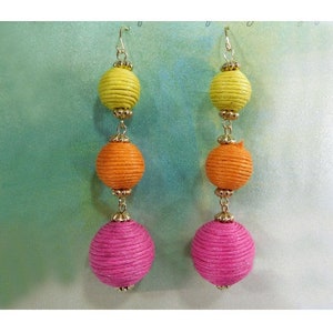 May include: A pair of long, dangling earrings with three round beads. The top bead is yellow, the middle bead is orange, and the bottom bead is pink.