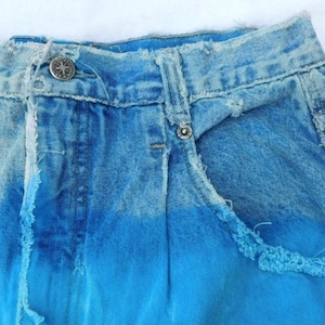 May include: A pair of blue denim shorts with a faded ombre effect, featuring a light blue to dark blue gradient. The shorts have a distressed look with frayed edges and a ripped pocket.