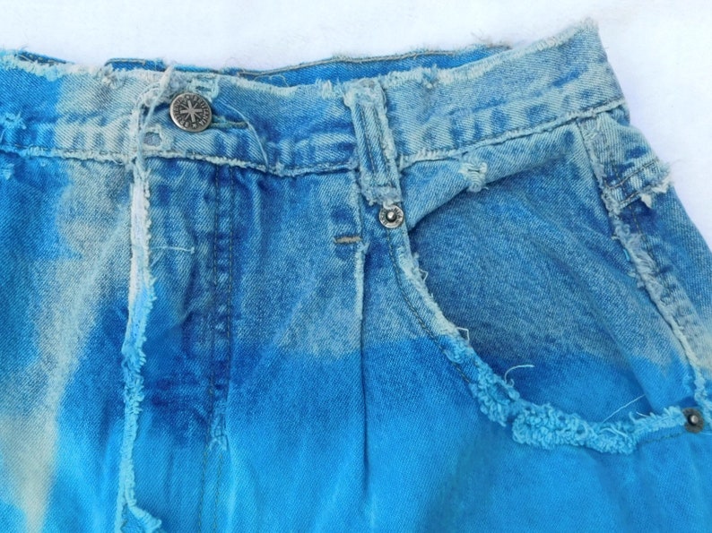 May include: A pair of blue denim shorts with a faded ombre effect, featuring a light blue to dark blue gradient. The shorts have a distressed look with frayed edges and a ripped pocket.