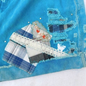 May include: A pair of blue denim shorts with patches of plaid fabric, lace, and a small embroidered design. The shorts have a distressed look with frayed edges.