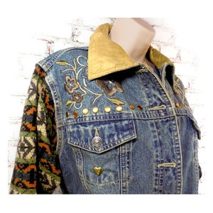 May include: A blue denim jacket with a brown suede collar, embroidered floral details, and gold studs. The jacket has a knitted sleeve with a brown, green, and orange pattern.