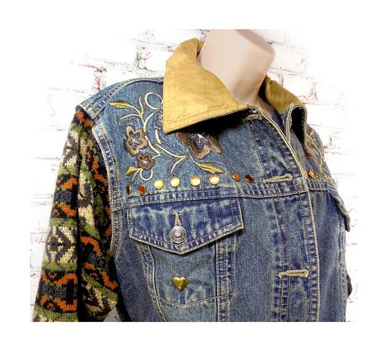 May include: A blue denim jacket with a brown suede collar, embroidered floral details, and gold studs. The jacket has a knitted sleeve with a brown, green, and orange pattern.