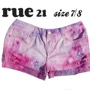 May include: Pink and purple tie-dye denim shorts with embroidered flowers. The shorts are distressed and have a frayed hem. The label reads "rue 21 size 7/8".
