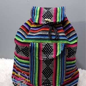 May include: A colorful striped backpack with a black base and a drawstring closure. The backpack is made of woven fabric and has a small pocket on the front.