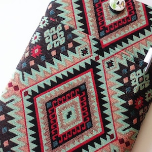 Könnte beinhalten: Ein schwarzer, roter und grüner Stoff mit geometrischem Muster. Der Stoff hat einen kleinen Knopf mit einem Vogelmotiv.