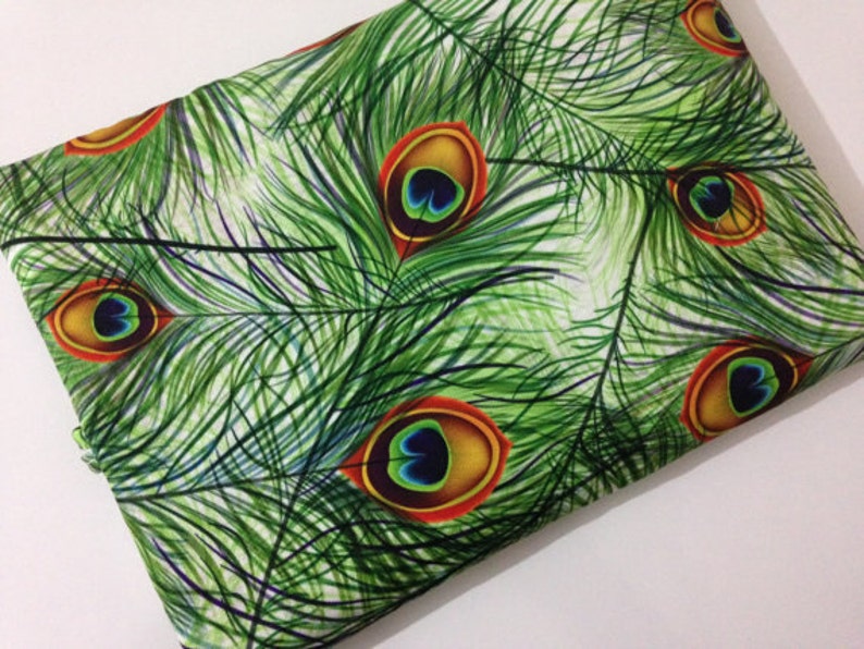 Pode incluir: Tecido branco com um padr&atilde;o de penas de pav&atilde;o verde e azul. As penas t&ecirc;m um olho vermelho, laranja e amarelo.