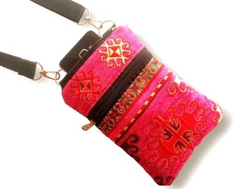 May include: A pink and red embroidered crossbody phone bag with a black strap. The bag features geometric patterns in gold and red, with a black zipper and a gold-colored zipper pull. The strap is black and adjustable.
