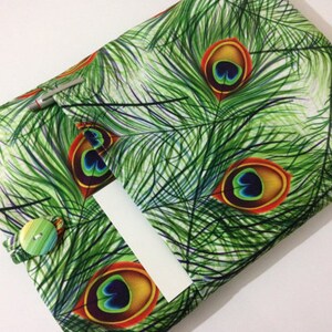 Pode incluir: Uma capa de livro de tecido verde com um padr&atilde;o de penas de pav&atilde;o. A capa tem um bolso na frente e um fecho de bot&atilde;o.
