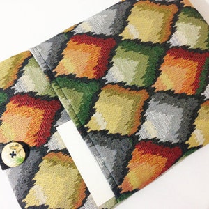 May include: A fabric clutch with a geometric pattern in shades of orange, green, gray, and black. The clutch has a flap closure with a button.