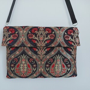 May include: A black fabric crossbody bag with a flap closure. The bag features a floral pattern in shades of red, pink, and gold on a dark blue background.