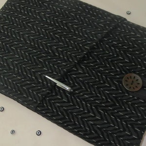 May include: A black fabric notebook cover with a silver pen and a decorative button. The cover has a chevron pattern.