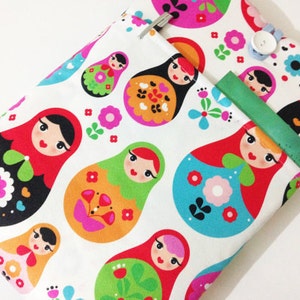 May include: A white fabric tablet case featuring a colourful pattern of Russian nesting dolls, flowers, and geometric shapes. The case has a pocket on the back for a pen or stylus.