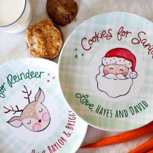 May include: Two green and white checkered ceramic plates with festive Christmas designs. One plate features a reindeer with the text "Cookies for Reindeer" and "Love, Baylor & Briggs". The other plate features Santa Claus with the text "Cookies for Santa" and "Love, Hayes and David".