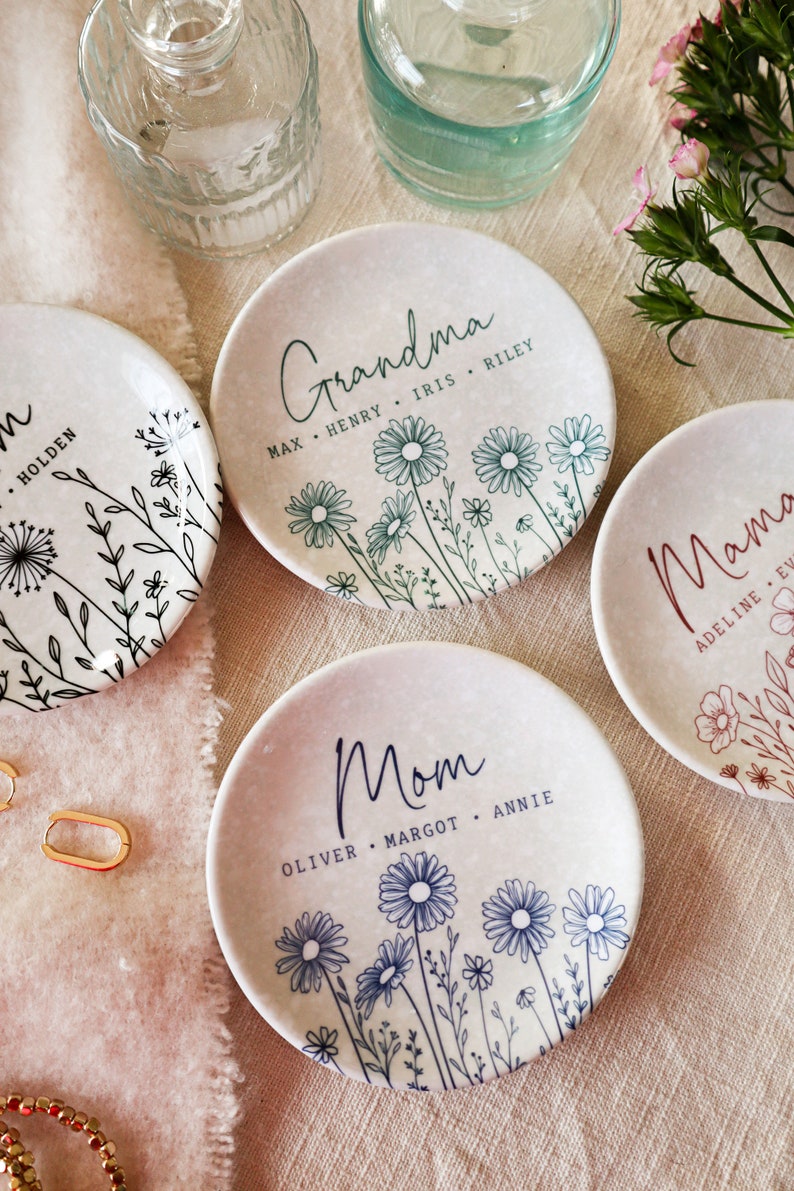 May include: Three ceramic ring dishes with floral designs and personalized text. The dishes are white with black, blue, and green floral designs. The text on the dishes reads "Grandma", "Mom", and "Mama" with the names of family members listed below.