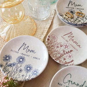 May include: Four ceramic trinket dishes with floral designs and personalized text. Each dish features a different floral pattern and the word "Mom", "Mama", or "Grandma" with names underneath.