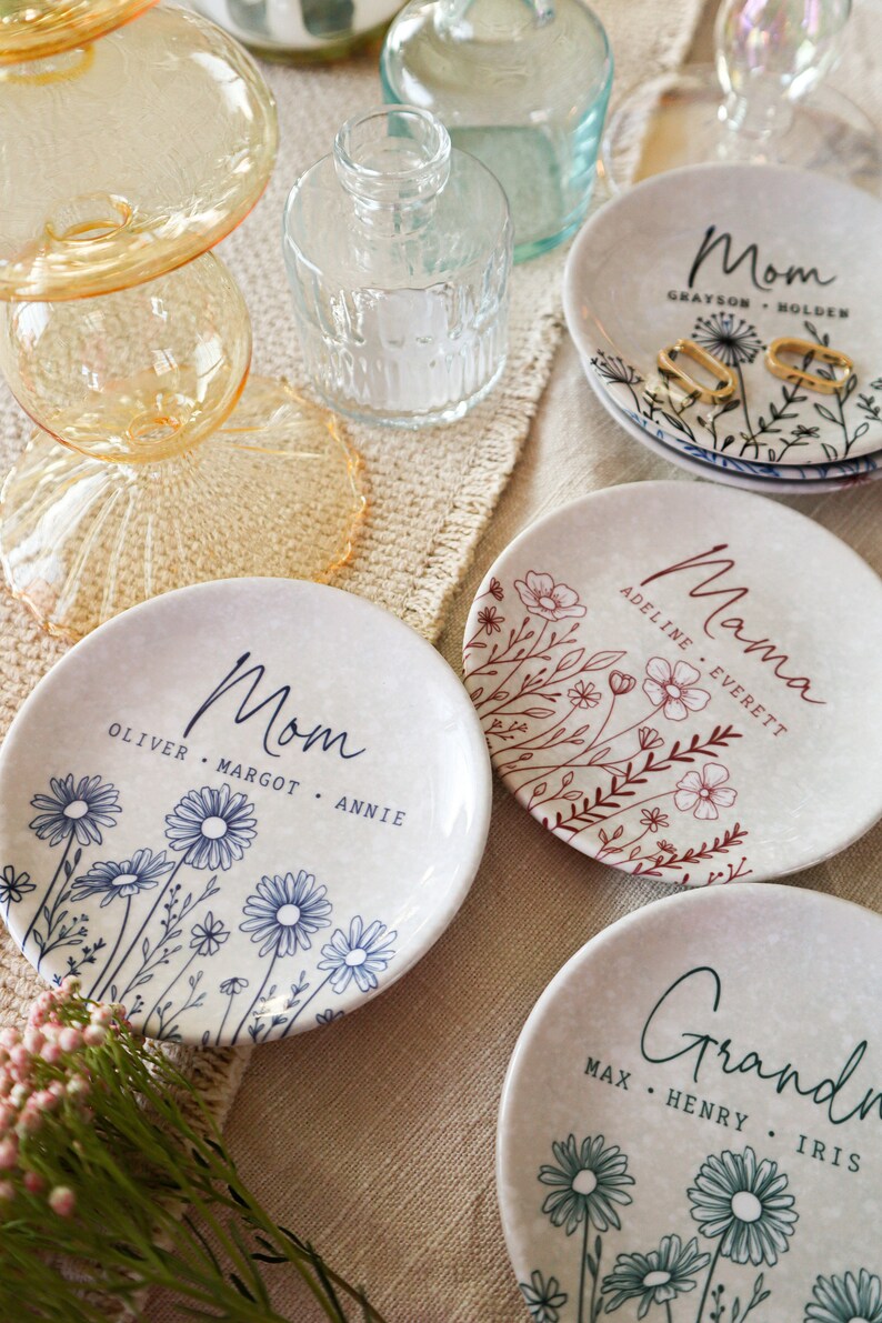 May include: Four ceramic trinket dishes with floral designs and personalized text. Each dish features a different floral pattern and the word "Mom", "Mama", or "Grandma" with names underneath.