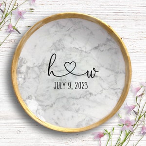 May include: A round, white marble-patterned tray with a gold-painted rim. The tray features the initials "h" and "w" connected by a heart, with the date "JULY 9, 2023" below. The tray is a decorative item.