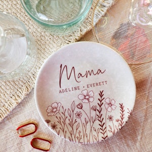 May include: A white ceramic trinket dish with a floral design and the text "Mama Adeline Everett" in brown lettering.