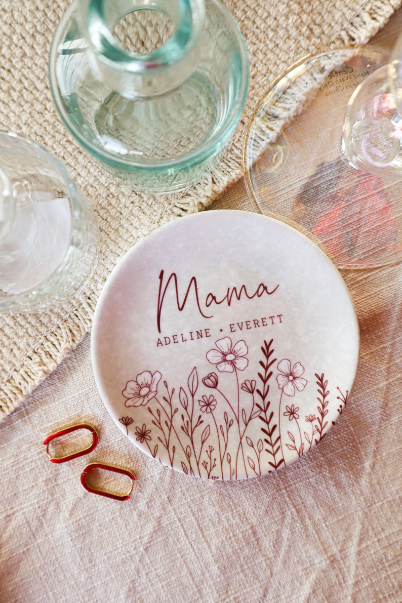 May include: A white ceramic trinket dish with a floral design and the text "Mama Adeline Everett" in brown lettering.