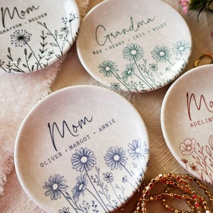 May include: Four white ceramic ring dishes with floral designs and personalized text. The dishes say "Mom", "Mom", "Grandma", and "Ma".