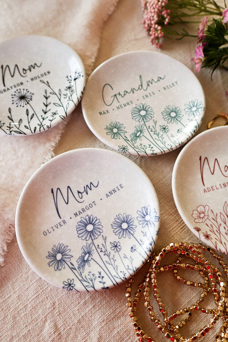 May include: Four white ceramic ring dishes with floral designs and personalized text. The dishes say "Mom", "Mom", "Grandma", and "Ma".