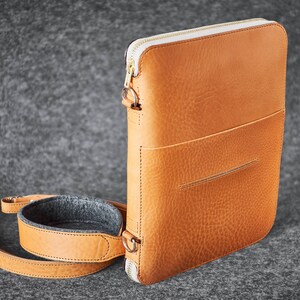 Può includere: Una borsa a tracolla in pelle marrone con una cerniera bianca e una tracolla rimovibile. La borsa ha una tasca frontale e uno scomparto principale.