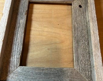 May include: A rustic wooden picture frame with a weathered gray and brown finish. The frame has a simple design with a rectangular opening for a picture.