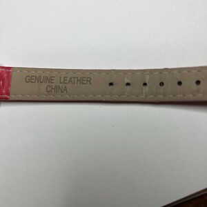 K&ouml;nnte beinhalten: Nahaufnahme eines roten Uhrenarmbands mit den Worten "GENUINE LEATHER CHINA" auf der Unterseite. Das Armband hat mehrere L&ouml;cher zur Anpassung.
